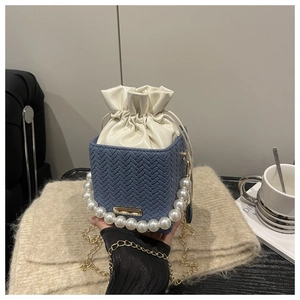 Détail d'un sac bleu tissé avec poignée en perles et bandoulière chaîne dorée