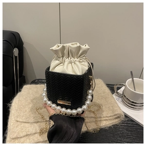 Détail d'un sac seau tressé noir avec poignée en perles et pochette à cordon