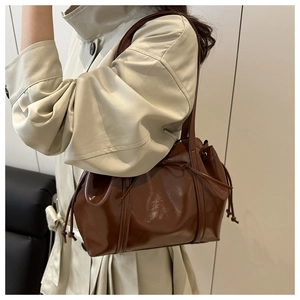 Close-up of a brown patent leather shoulder bag with a drawstring bow on a beige coat