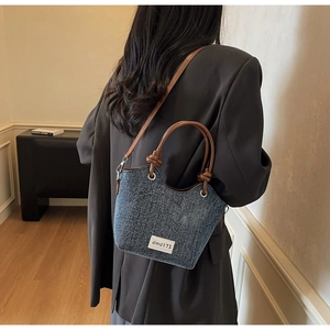 Vista posteriore della borsa a secchiello in denim blu con cinturini in pelle marrone