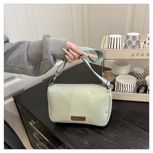 Détail d'un sac bandoulière vert clair avec étiquette en cuir et large sangle en nylon