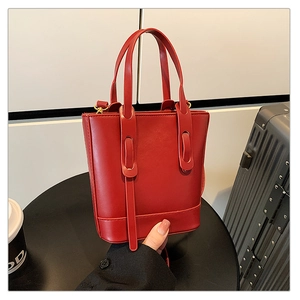Détail du sac seau rouge minimaliste avec doubles poignées et accents de métal doré