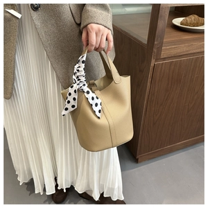 Beige pebble leather bucket bag styled with a polka dot scarf in a warm lifestyle setting