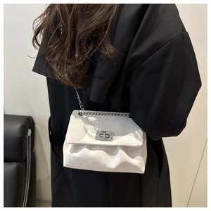 Detailed view of white pleated chain bag with diamond buckle worn on black coat