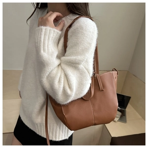 Brown leather tote bag with white contrast stitching carried by a model in a white sweater