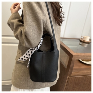 Close-up of black leather bucket bag featuring pebbled texture and polka dot scarf detail