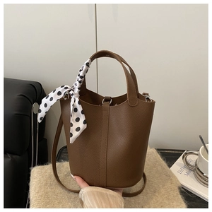 Détail du sac seau en cuir marron avec foulard à pois sur fond de laine tissée