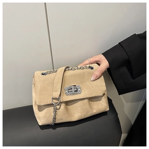 Close-up of beige suede handbag featuring a luxury rhinestone swivel lock and silver chain
