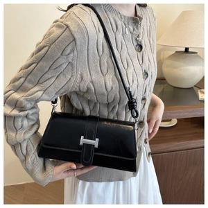 Close-up of a black glossy leather baguette bag with a stylish silver metal buckle