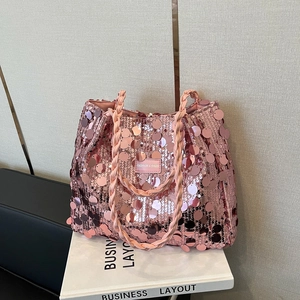 Pink sequin tote bag with woven handles shown on a white prop book with a grey background