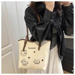 Model wearing a cream tote bag with cute cat illustrations and brown shoulder strap