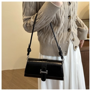 Close-up of black glossy leather shoulder bag with silver buckle on beige sweater