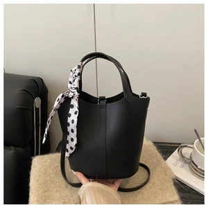 Détail du sac seau en cuir grainé noir avec un foulard à pois élégant sur la poignée