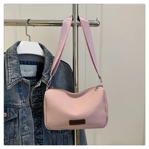 Détail du sac à bandoulière en toile rose avec étiquette en cuir et fermeture éclair