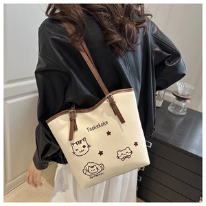 Detail of cream tote bag featuring cat illustrations and adjustable brown leather straps
