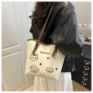 Close-up of cream leather tote bag with cute cat illustrations and brown shoulder strap