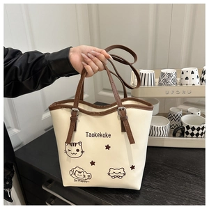 Close-up of a cream tote bag featuring a cute cartoon cat illustration and brown straps