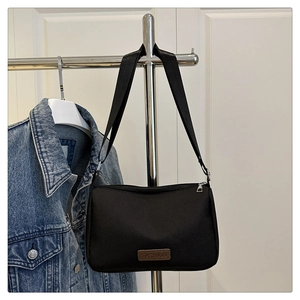 Détail d'un sac à bandoulière en nylon noir avec logo en cuir marron sur un cintre