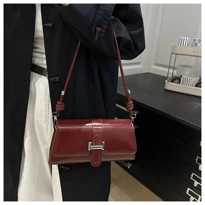 Detail of burgundy leather baguette bag with silver metal buckle and knotted strap