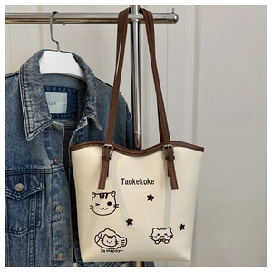Detail of cream bucket bag featuring cute cat print and adjustable brown shoulder strap