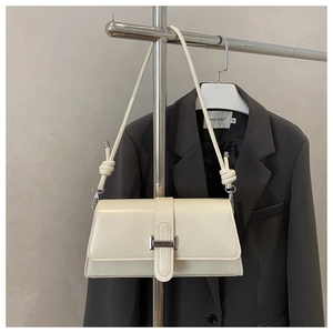 Detail of cream baguette bag with silver rectangle clasp and knotted shoulder strap