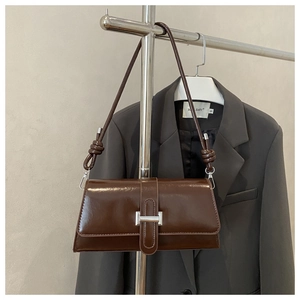 Detail of a brown leather baguette bag with silver buckle and knot strap on a blazer