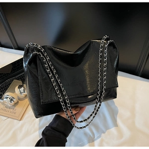 Detail of black glossy crinkled leather tote bag with silver metal chain shoulder strap