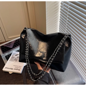 Close-up of black glossy tote bag with silver chain strap and wrinkled texture
