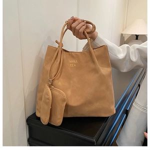 Close-up of tan suede tote bag featuring minimalist lettering and a matching charm pouch