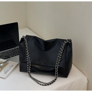 Detail of black tote bag with wrinkled texture, silver chain strap, and flap design