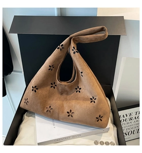 Macro detail of brown suede tote bag with floral cutout patterns in a gift box