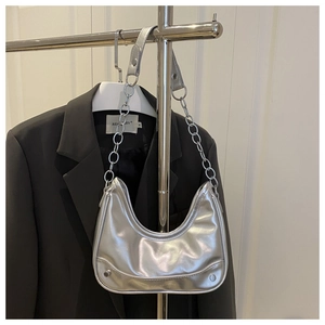 Detail of silver metallic crescent bag with chain strap against a black suit jacket