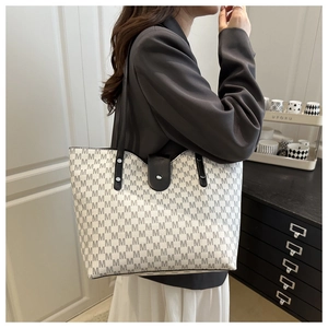 Side view of model wearing a large cream tote bag with grey M-pattern print and black straps