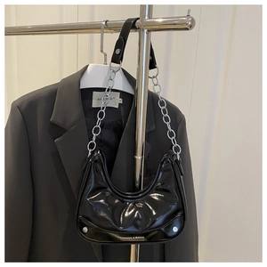 Detail of black glossy patent leather hobo bag with silver chain strap and metal logo