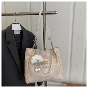 Detalle de bolso tote jacquard beige con cadenas metálicas, perlas y colgante de nube