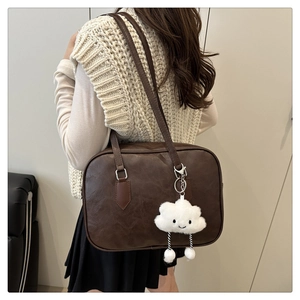 Brown retro bowling bag with white cloud pendant on shoulder of a model in a minimal setting