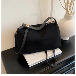 Detail of black suede tote bag with golden hardware on a decorative book and vase