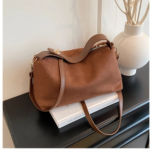 Detail of dark brown suede shoulder bag with gold hardware on a minimalist background