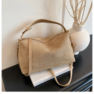 Detail of khaki suede tote bag with metal zipper and adjustable strap on a book