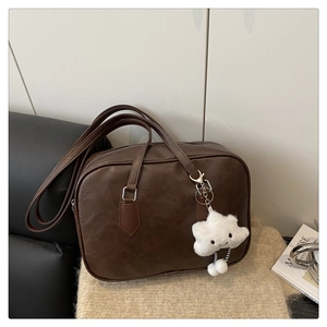 Close-up of dark brown faux leather bag with silver hardware and white plush charm