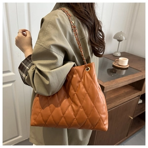 Detail of caramel quilted tote bag featuring golden chain strap and leather texture