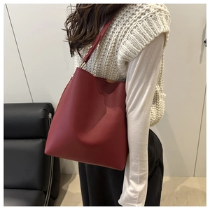 Minimalist red leather bucket bag with gold hardware shown on shoulder in a modern room