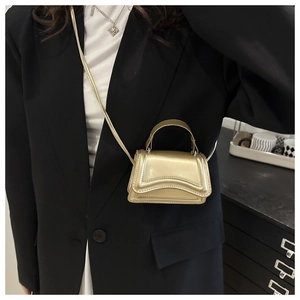 Detailed close-up of a metallic gold mini crossbody bag with a curved flap design