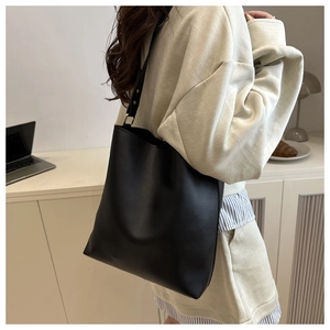 Detail of a minimalist black bucket shoulder bag with adjustable strap and metal buckle