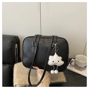 Detail of a black leather tote bag with white cloud plush pendant on a cozy sofa