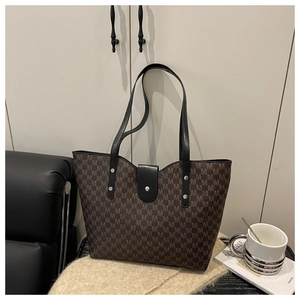 Detail of a brown monogram tote bag with black leather straps and silver metal studs