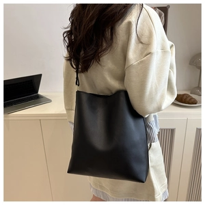 Detail view of the black minimalist PU leather bucket bag worn over a woman shoulder