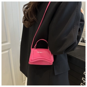 Vue détaillée du mini sac en cuir verni fuchsia porté sur un blazer noir élégant