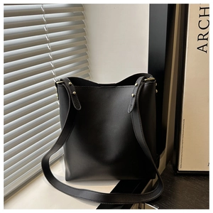 Close-up of a black leather bucket bag featuring gold stud detail in natural window light