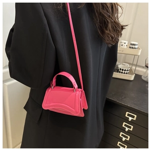 Détail du sac à main sablier en cuir verni rose porté avec un blazer noir